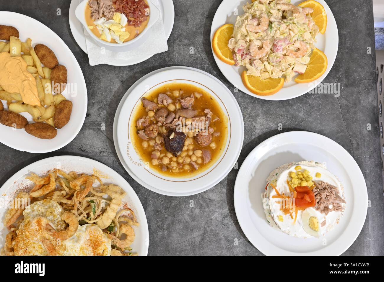 A table with a variety of food, including a cake. The table is set with plates and bowls of different sizes and shapes Stock Photo
