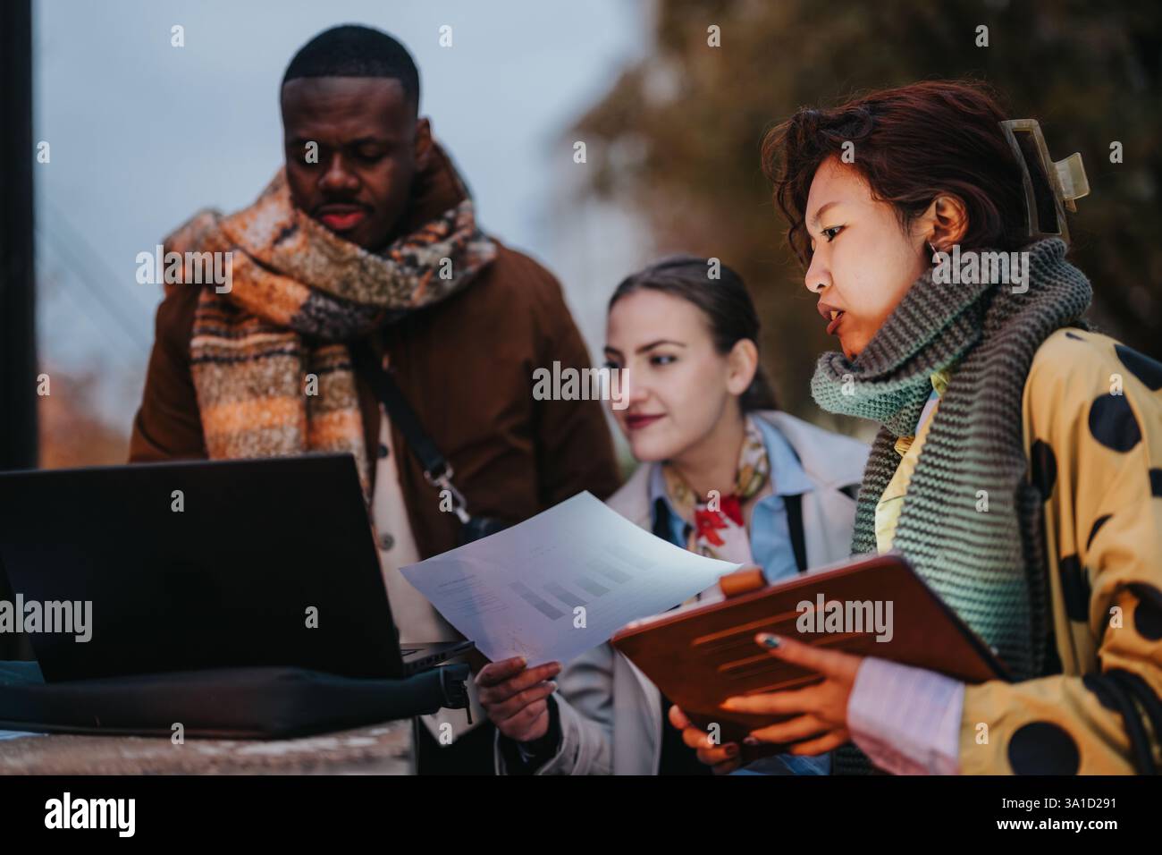 Multiracial people collaborating outdoors with documents and a laptop Stock Photo