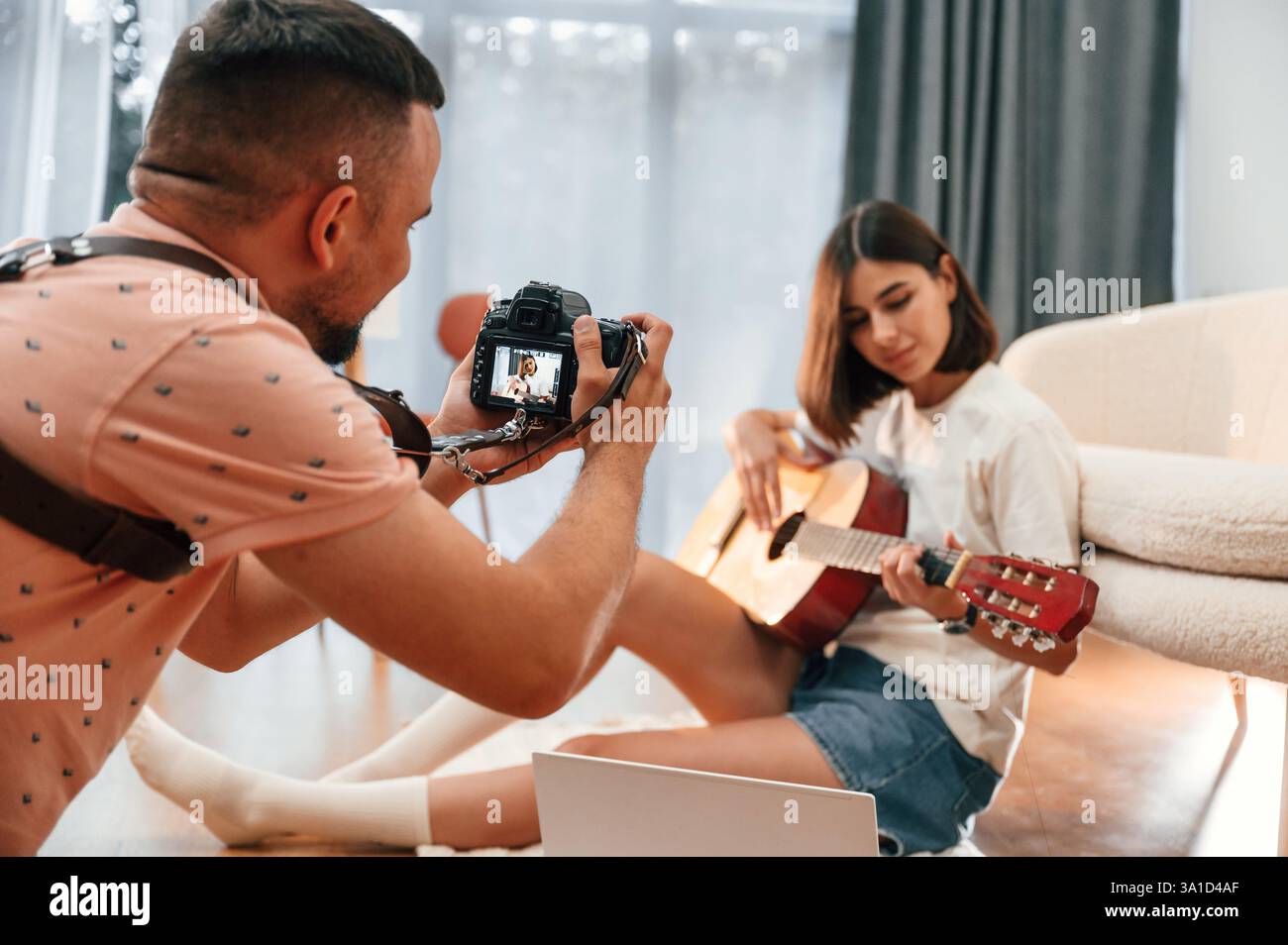 Photographer is working, using camera. Beautiful woman in casual clothes is at home with guitar. Stock Photo