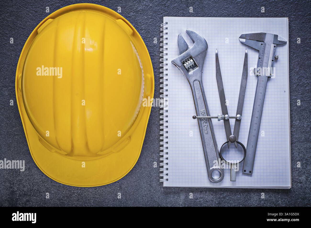 Notebook building helmet adjustable wrench divider calliper on black background Stock Photo