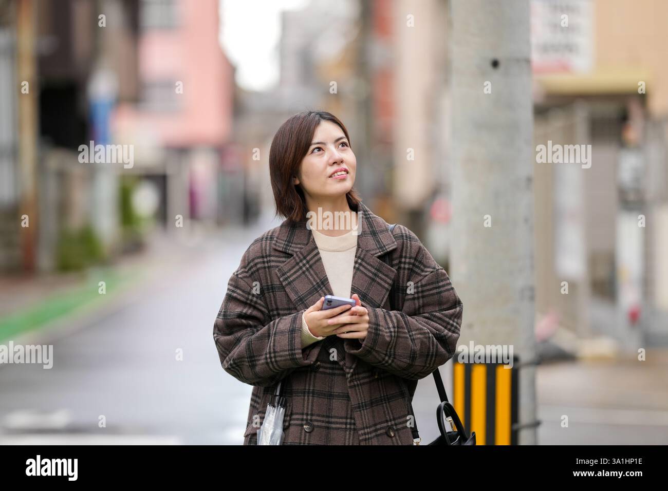 A 29-year-old Japanese woman wearing a checkered coat. She walks through alleys with few Japanese cars in her hand. Stock Photo
