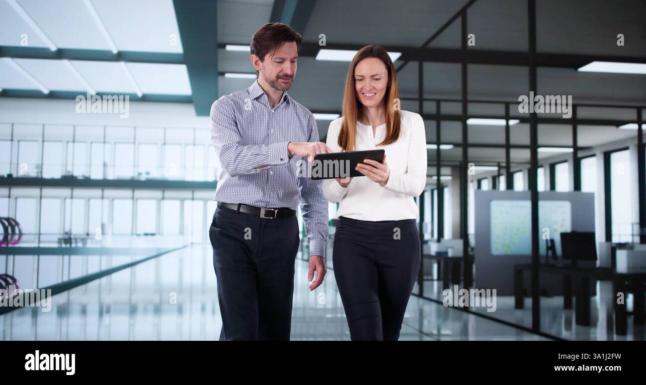 Happy Workplace Conversation: Two colleagues walk and talk with tablet Stock Photo