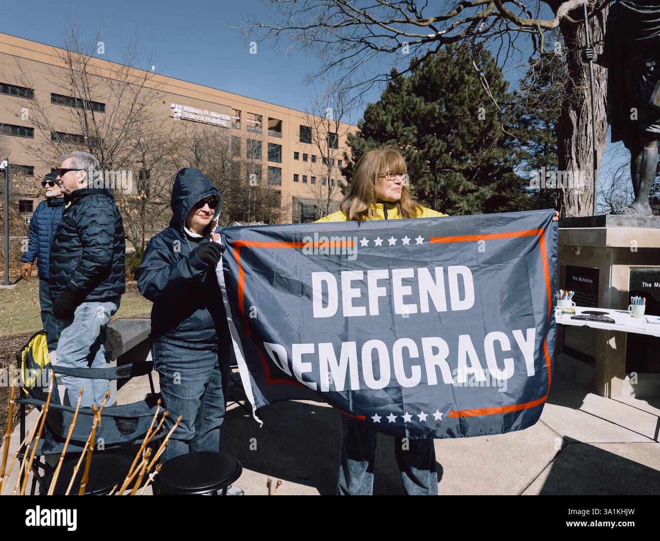 Women holding a flag reading Defend Democracy, at the International Women's Day Rally, Flint Michigan USA, March 8 2025 - Smartphone Captured Stock Image