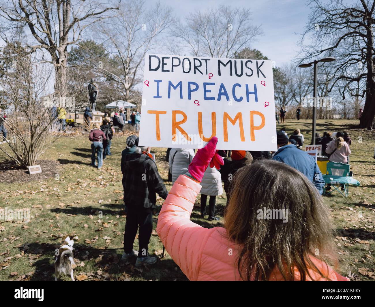 A woman holds a sign reading Deport Musk Impeach Trump at the International Women's Day rally in Flint Michigan USA, March 8 2025 - Smartphone Captured Stock Image