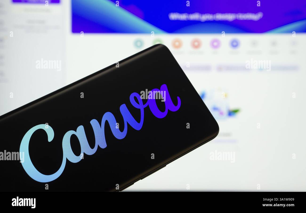 Canva logo is displayed on a smartphone screen, with the canva website visible on a computer screen in the background Stock Photo