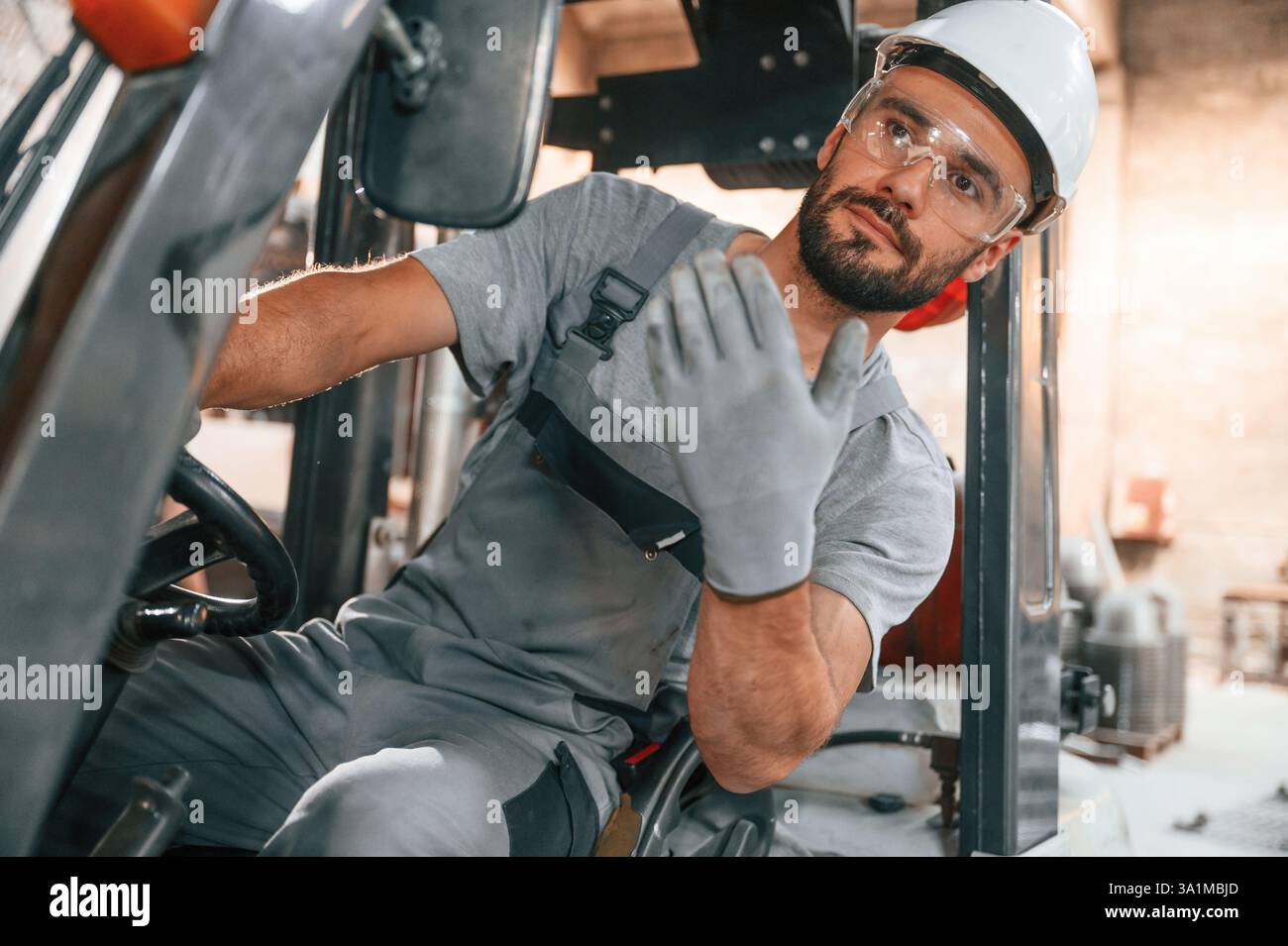 Hand gestures. In the forklift. Young factory worker in grey uniform ...