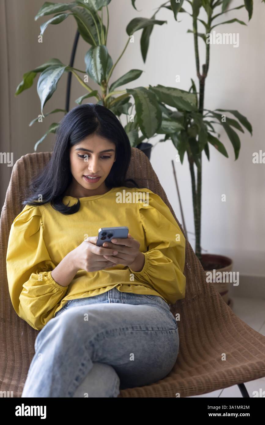 Pretty Indian woman relaxing on armchair with smartphone Stock Photo ...