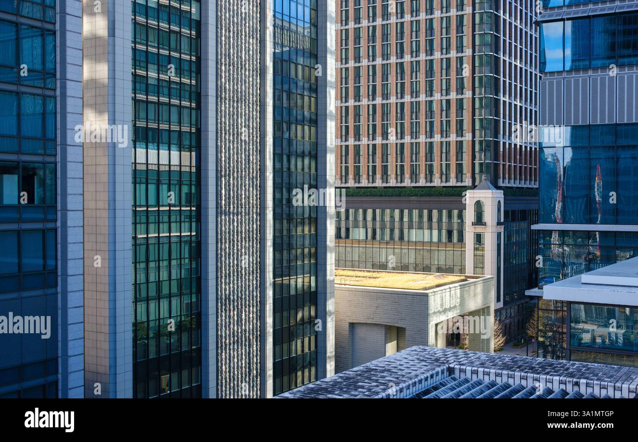 A cluster of modern office buildings in Tokyo, Japan, featuring sleek glass facades, geometric architectural patterns, and reflective surfaces. The mi Stock Photo