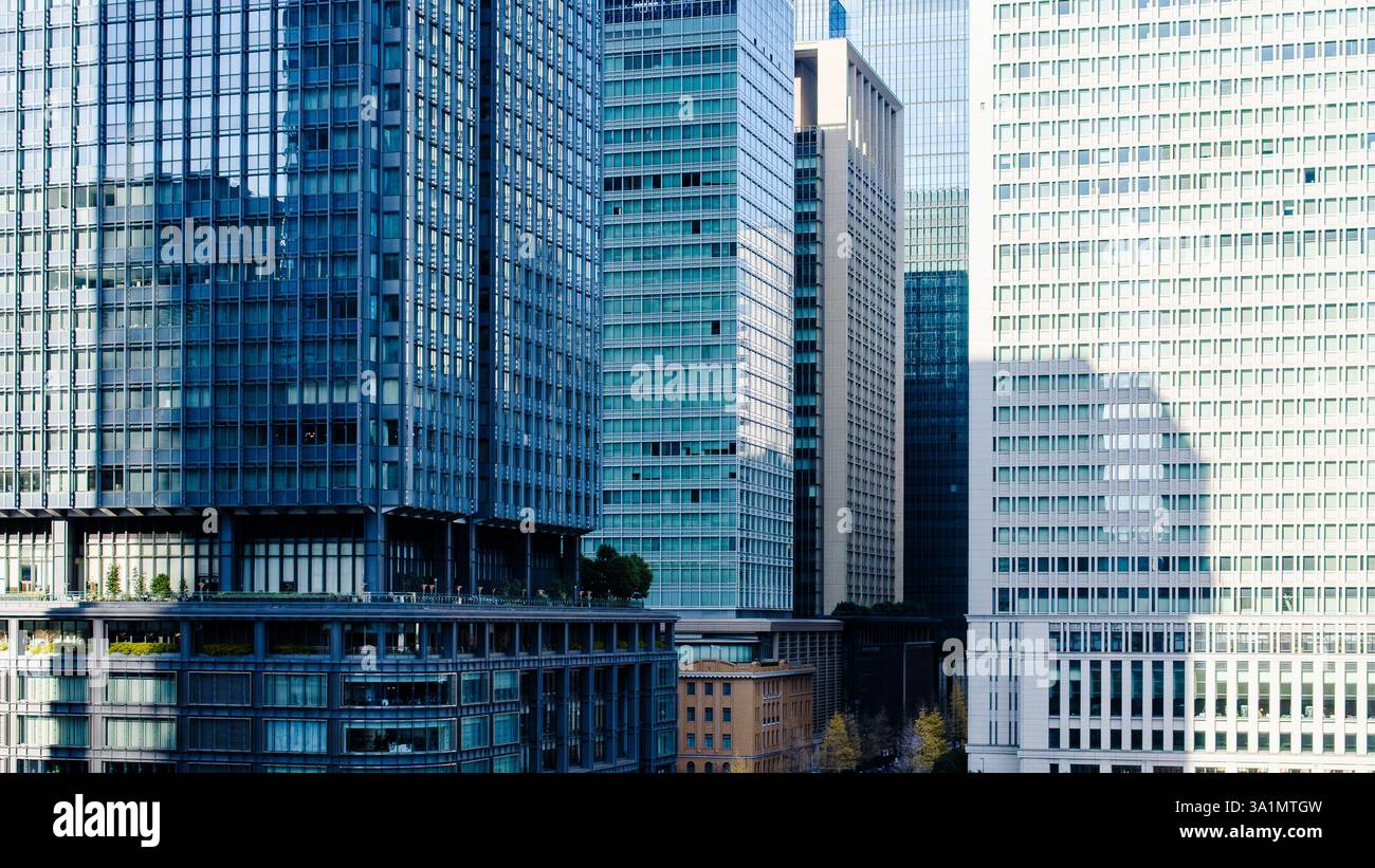 A cluster of modern office buildings in Tokyo, Japan, featuring sleek glass facades, geometric architectural patterns, and reflective surfaces. The mi Stock Photo
