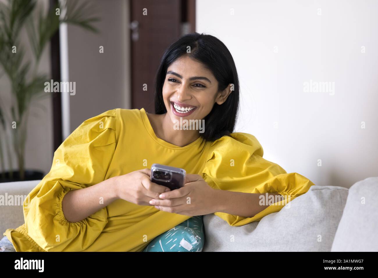 Happy Indian woman relaxing on sofa at home with smartphone Stock Photo ...