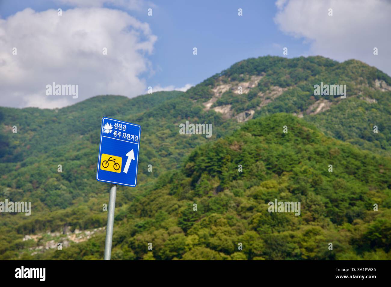 Sunchang County, South Korea - October 4, 2021: A blue sign marks the Seomjingang Bike Path’s route towards Chungju, standing against the lush, rocky Stock Photo