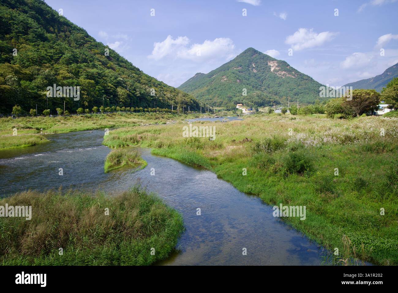 Sunchang County, South Korea - October 4, 2021: A winding stream flows into the Seomjin River, surrounded by lush grasslands and forested mountains un Stock Photo
