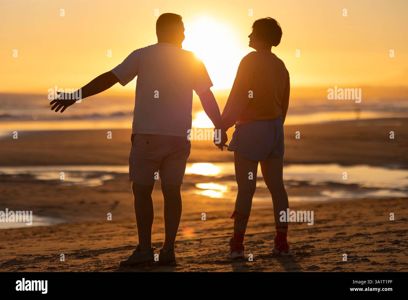 Couple holding hands and admiring golden sunset on beach Stock Photo ...