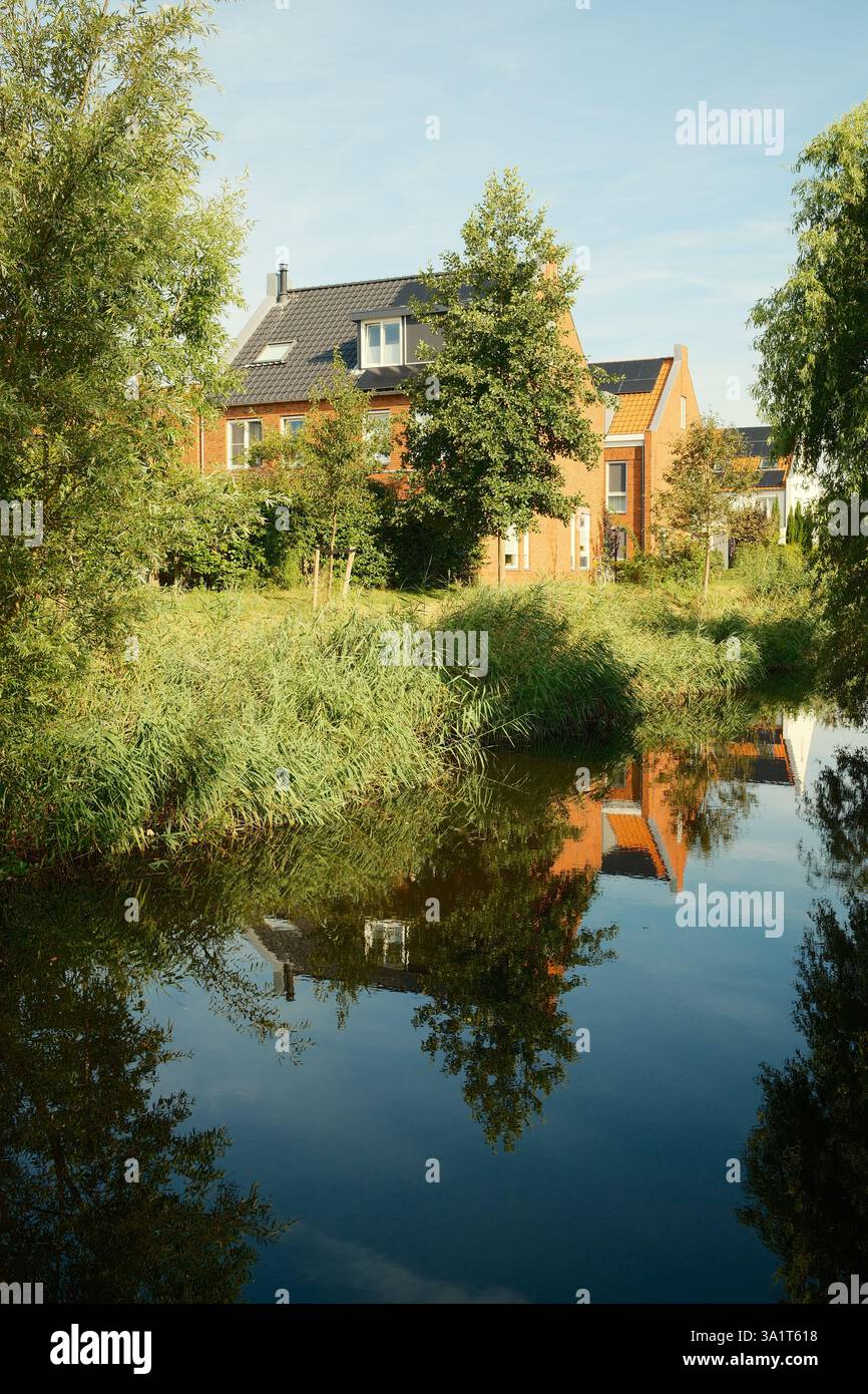 Modern houses reflecting in canal water with lush green vegetation Stock Photo
