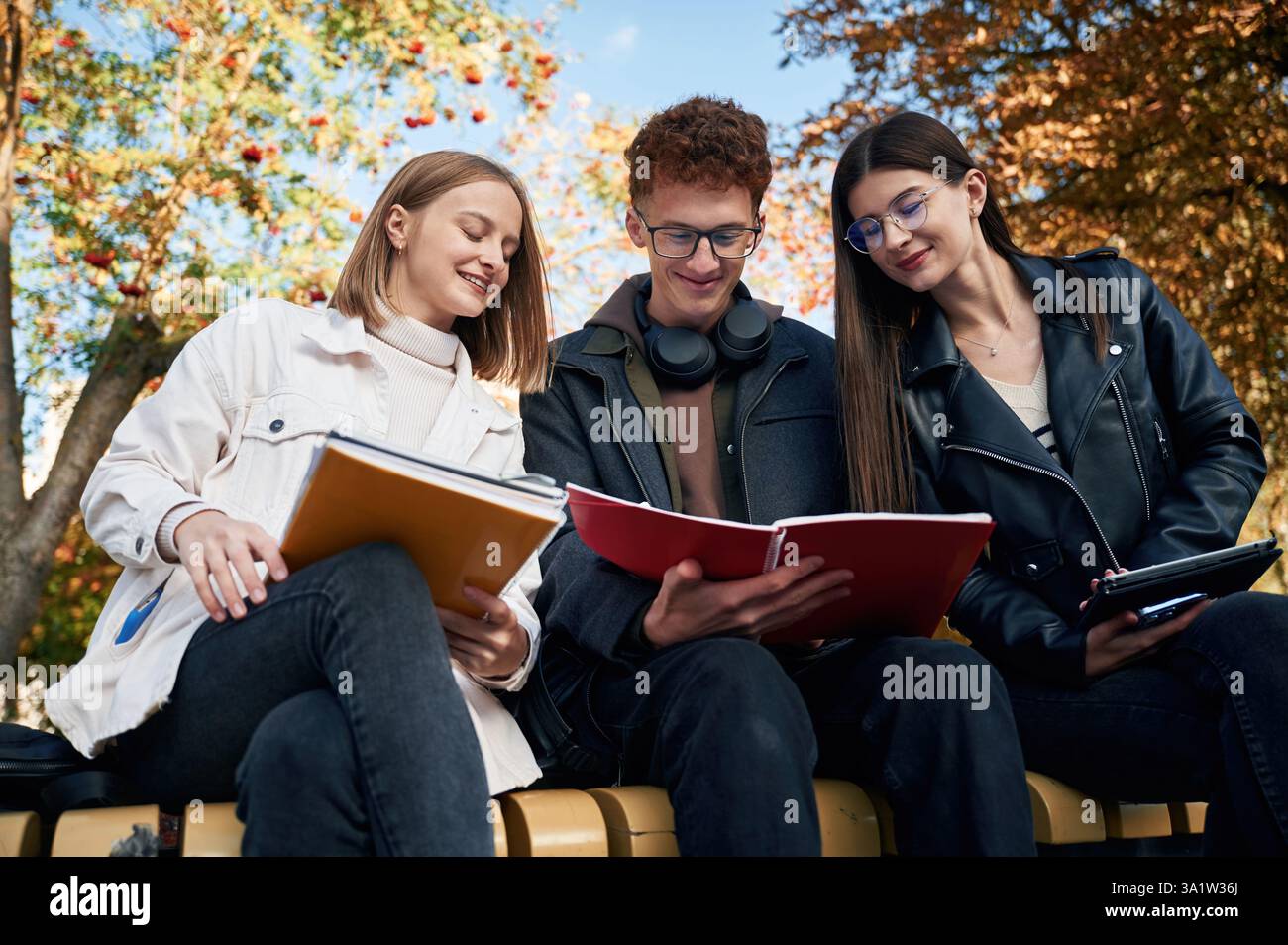 Three young students are outside the university outdoors. Stock Photo