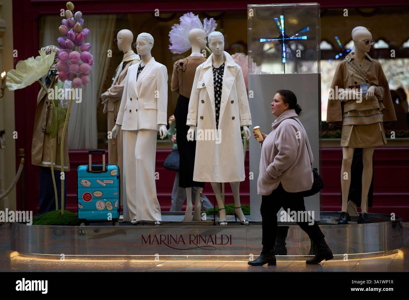 A woman eats an ice-cream walking past mannequins inside the GUM