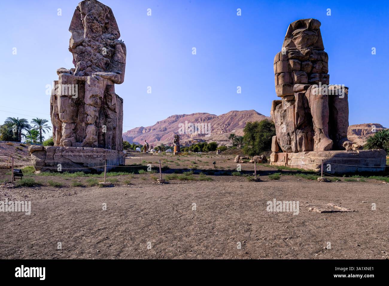 The Colossi of Memnon are two massive stone statues of the Pharaoh Amenhotep III, which stand in front of the ruined Mortuary Temple of Amenhotep III Stock Photo