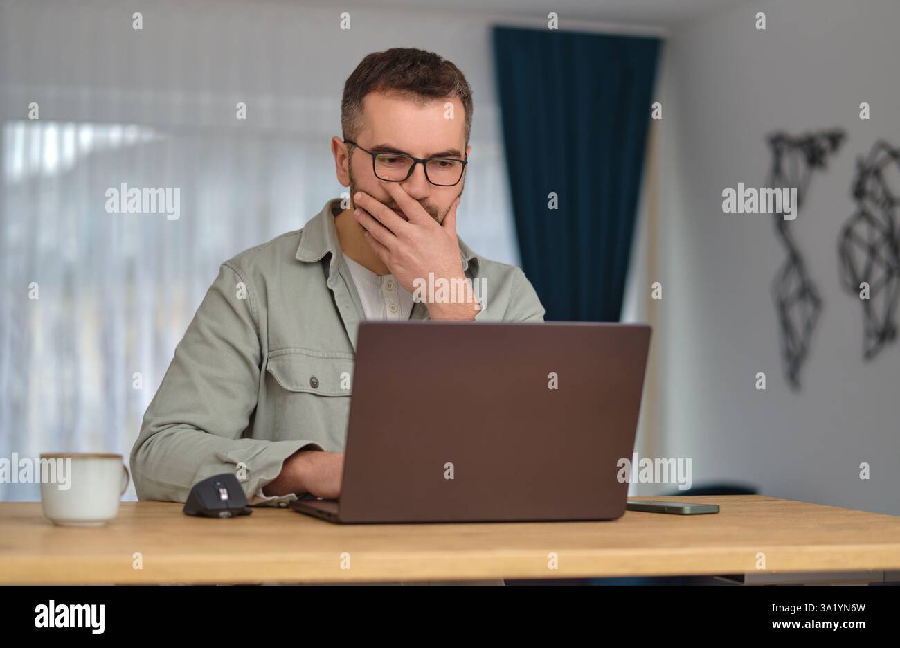 A worried man using a laptop while working at home office. Stock Photo