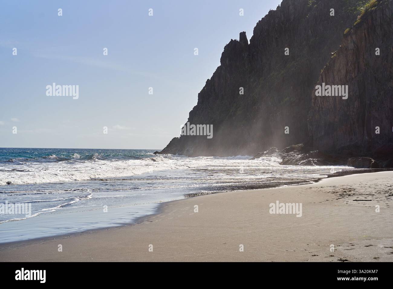 Black sand beach with ocean waves and towering misty cliffs under ...