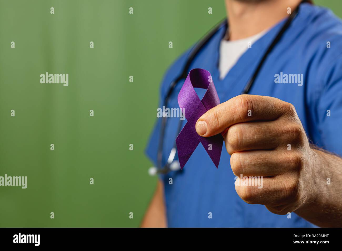 A healthcare worker wearing blue scrubs holds a purple ribbon in front ...
