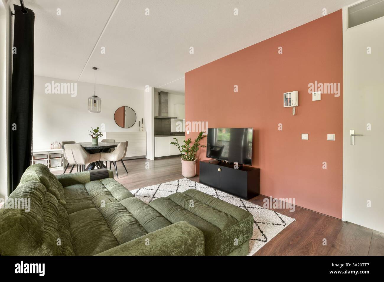 A contemporary living room featuring a cozy green sofa, television unit, and minimalist dining area. This space combines elegance and comfort with chic designs. Stock Photo