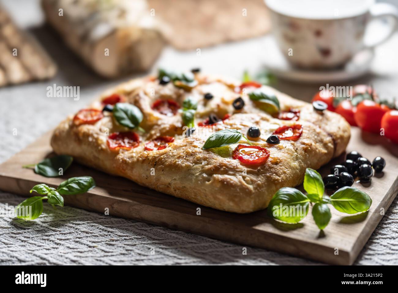 Focaccia - Italian Bread with tomatoes basil leaves olives and olive oil on cutting board. Stock Photo
