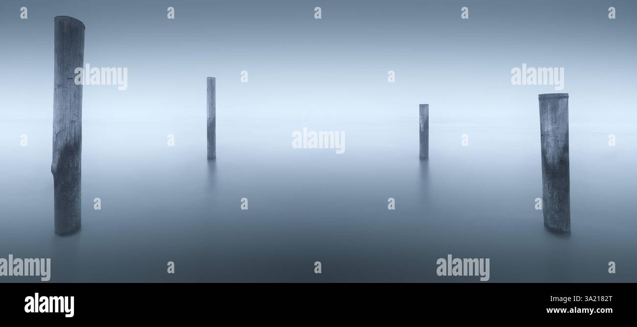 A minimalistic and monochrome image of a seascape with fog and poles in the water. Stock Photo