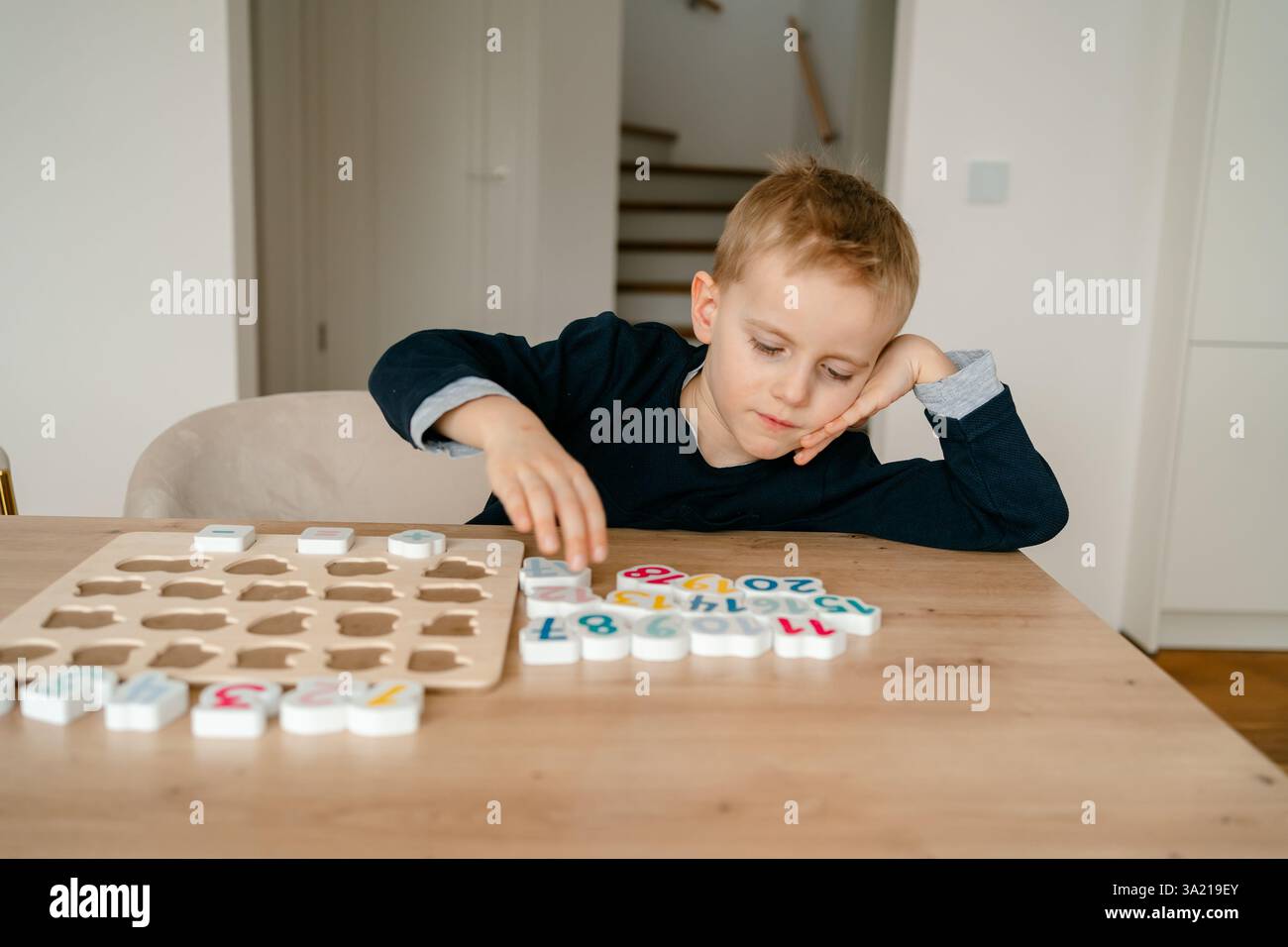 boy learns to count by laying out numbers from 1 to 20 on the board, boy 4-5 years old European appearance, at home in the living room sitting at the Stock Photo