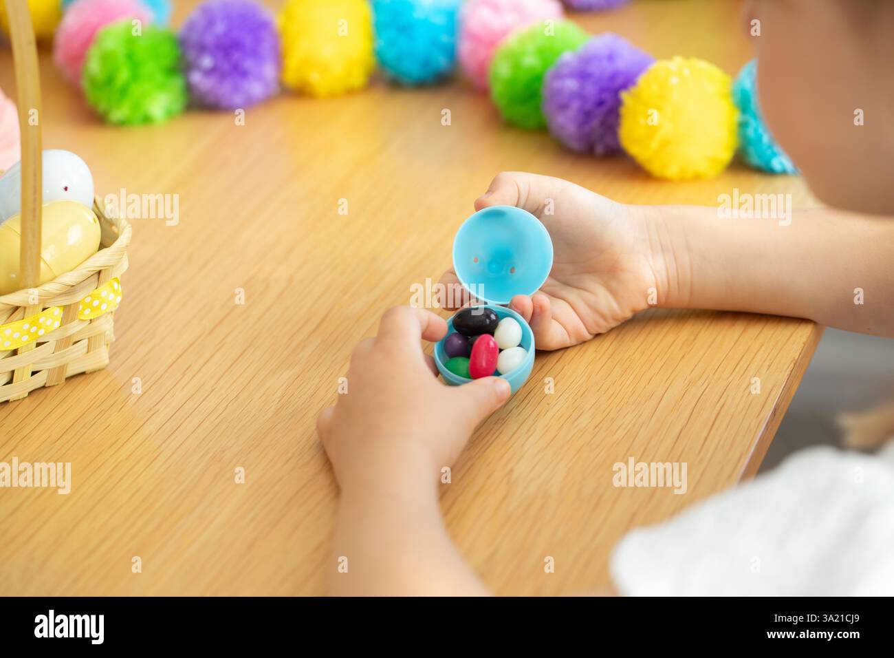 Child opening easter egg with colorful candy surrounded by festive decorations for spring celebration. Easter. Stock Photo