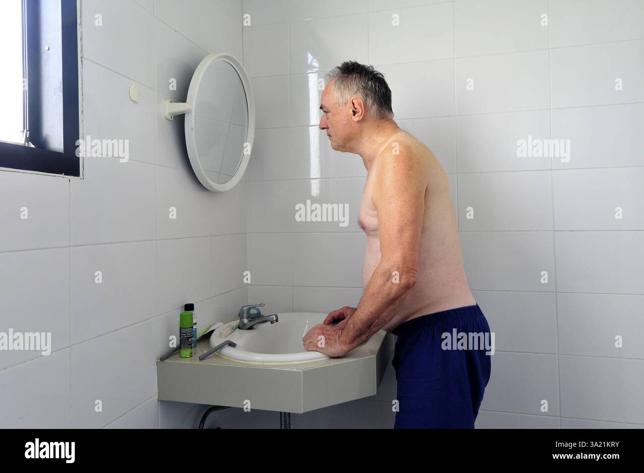 Man 60 plus looks at himself in the bathroom mirror Stock Photo