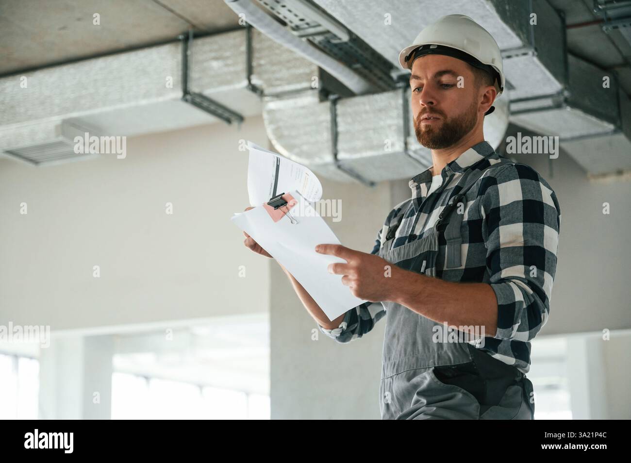 Checking the ceiling. Construction worker in uniform in empty unfinished room. Stock Photo