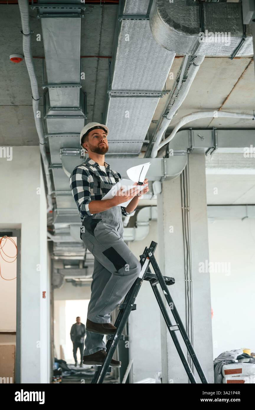 Checking the ceiling. Construction worker in uniform in empty unfinished room. Stock Photo