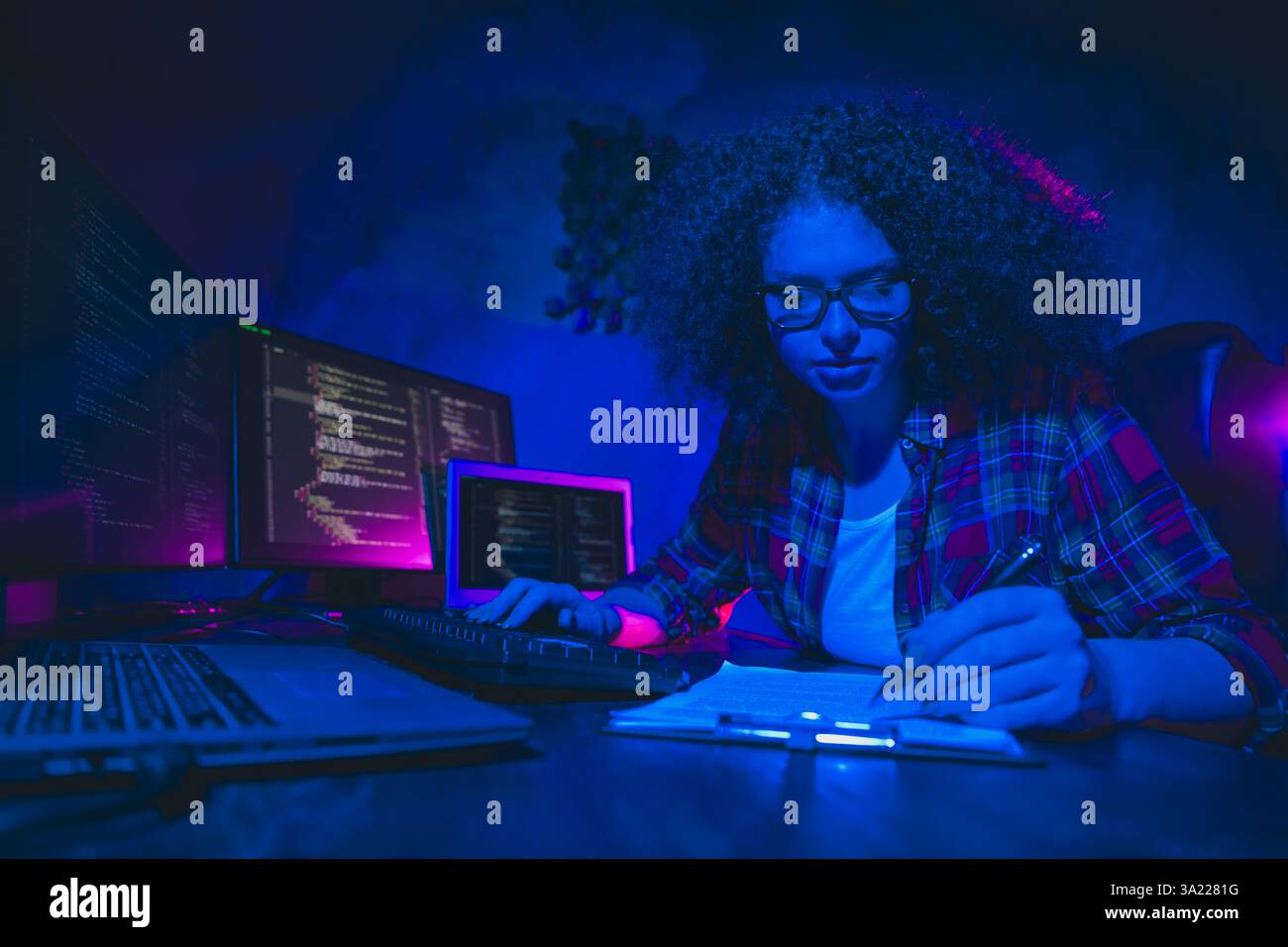 Young female programmer working on code in a modern workspace with multiple monitors, showcasing focus Stock Photo