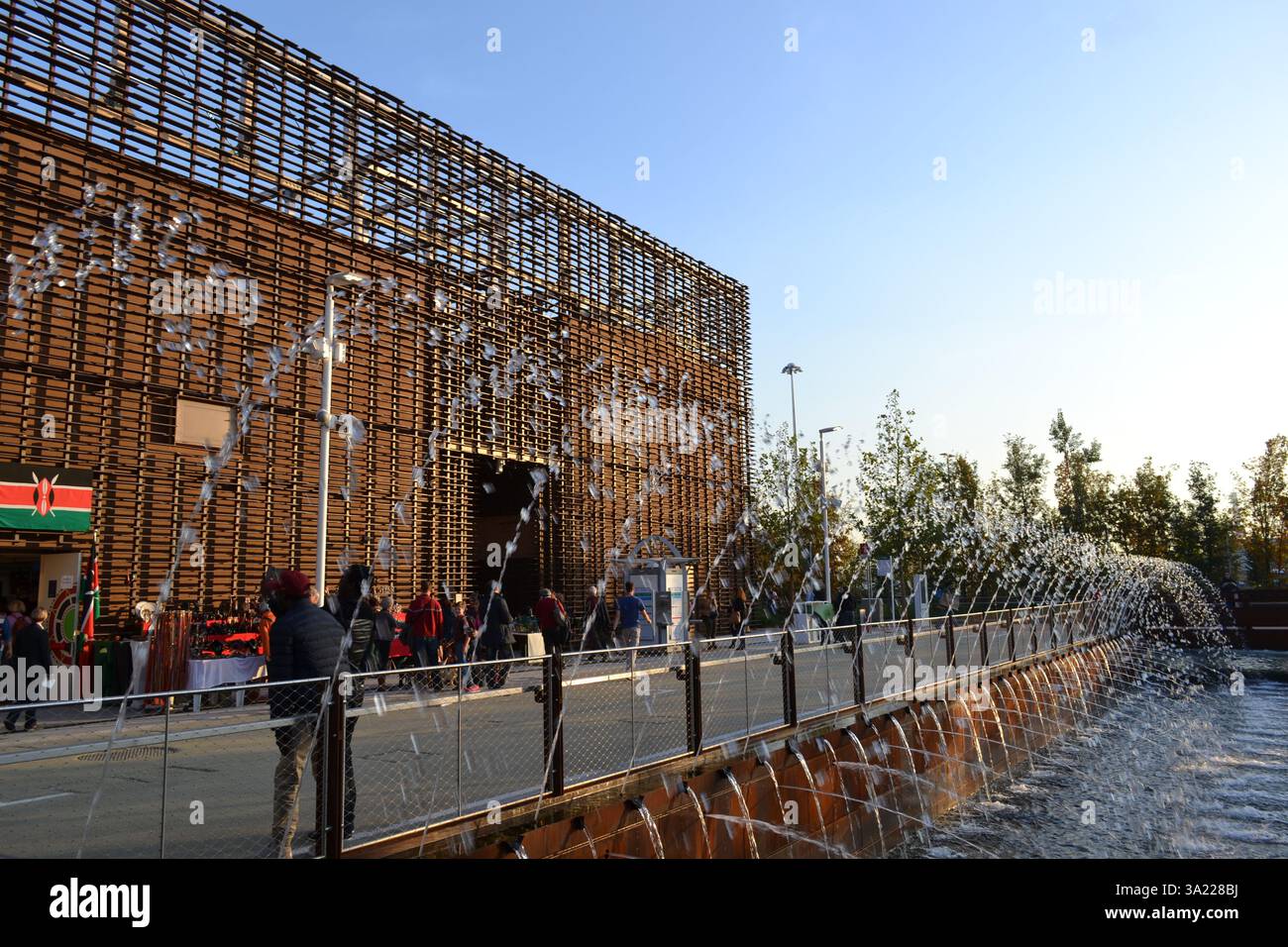 Water jets of fountain into the pool outside the Coffee cluster pavilion of the EXPO Milano 2015 at sunny sunset. Wooden air-conditioned pavilion. Stock Photo