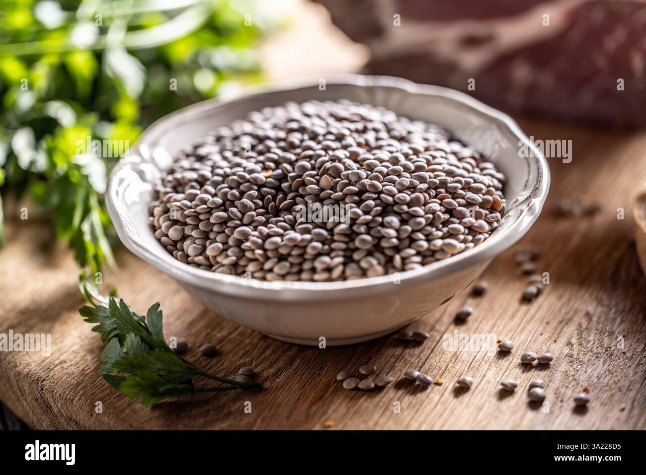Raw lentils in bowle with parsley herbs on kitchen table. Stock Photo