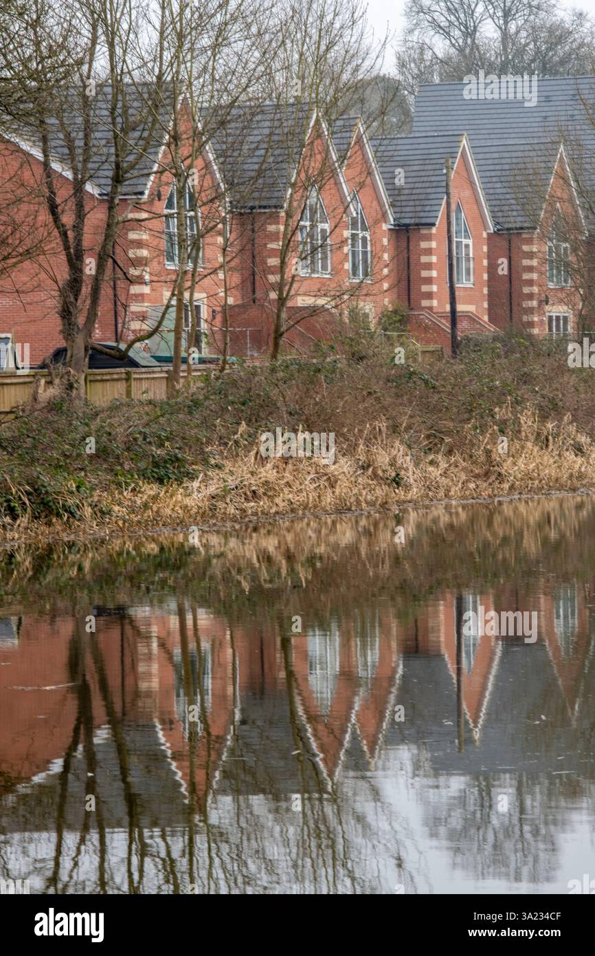 modern new-build homes and houses reflected in the canal on the water's ...