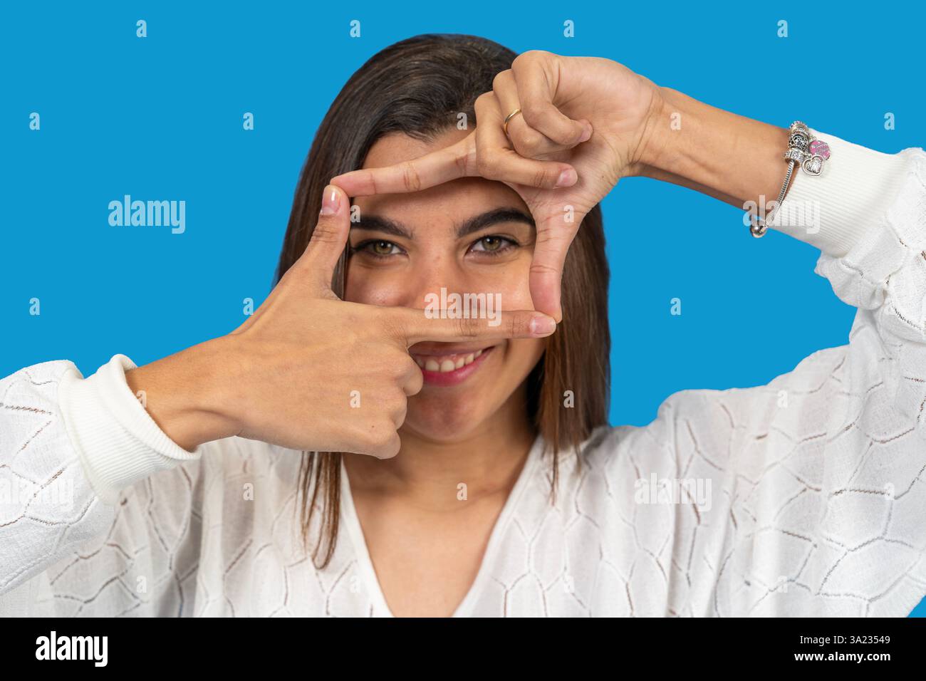 Young woman framing her face with fingers on blue background Stock Photo