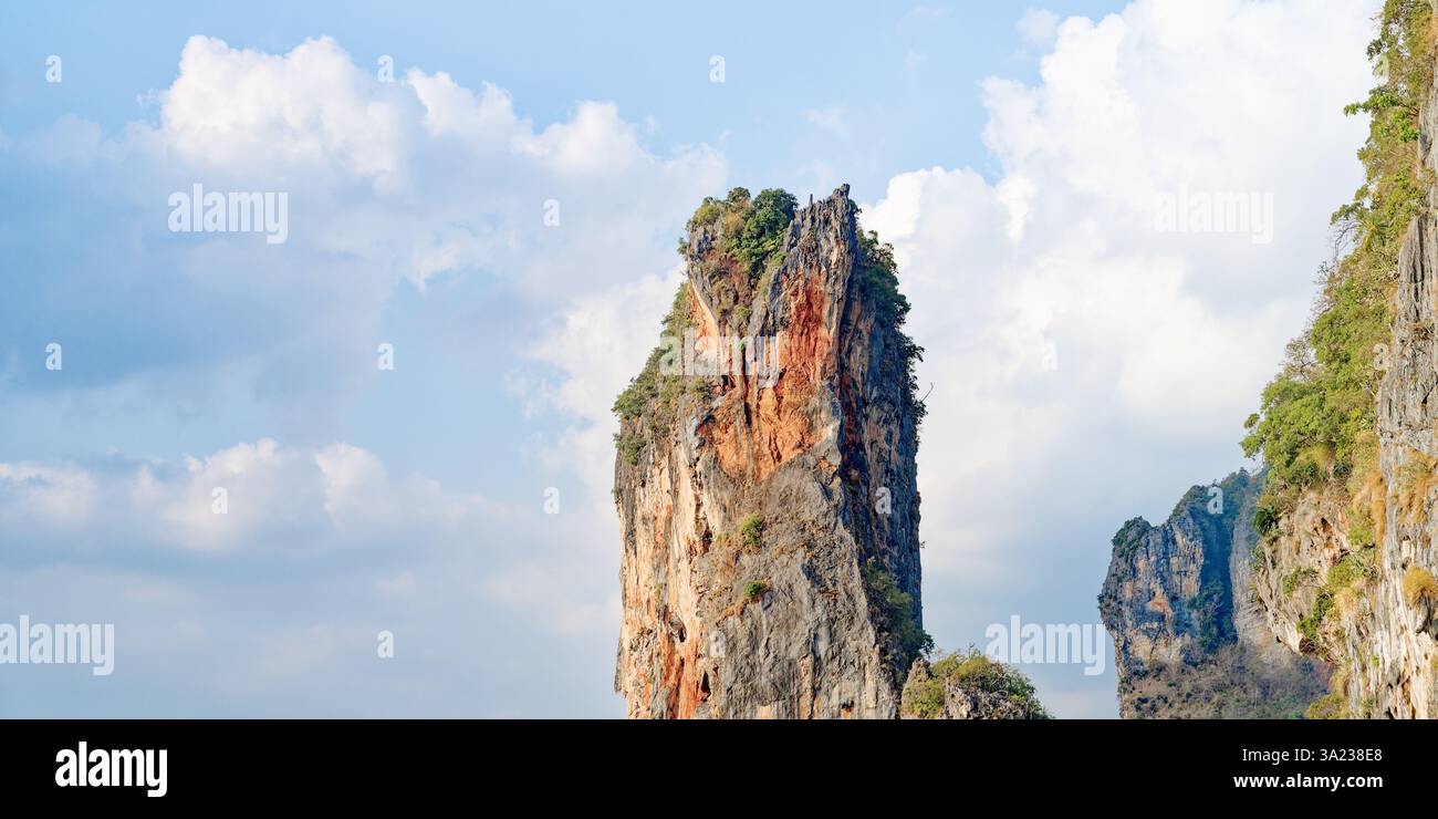 A towering limestone cliff stands against a backdrop of soft clouds ...