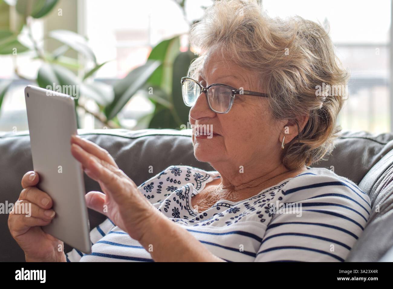 Senior woman sitting on couch at home using wireless tablet Stock Photo