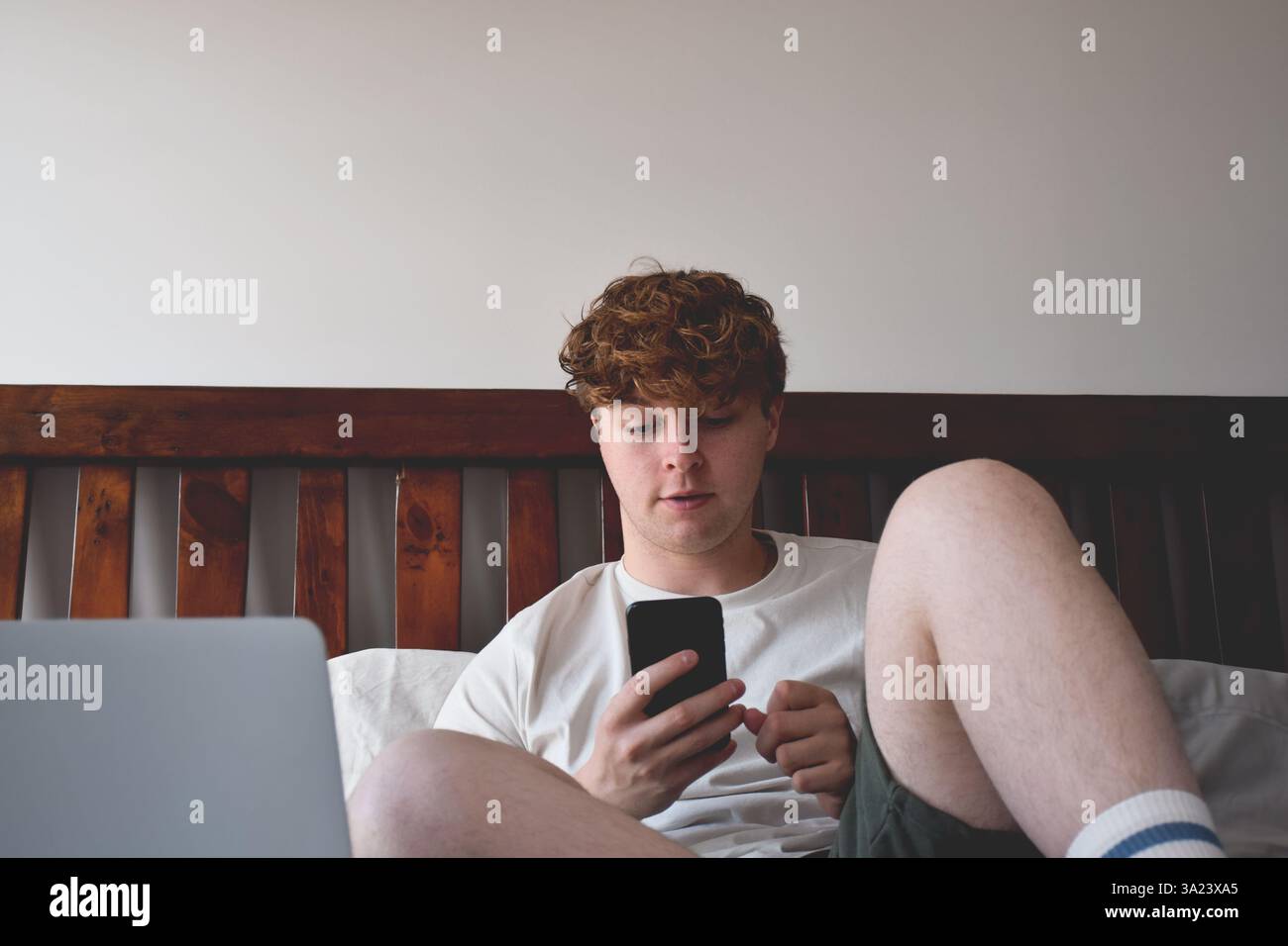Young man sitting on bed using mobile phone Stock Photo
