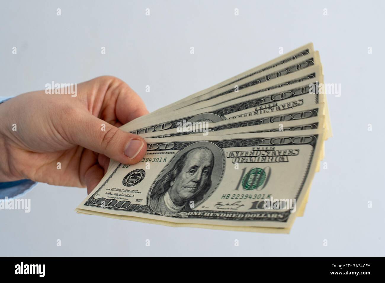 Close-up of male hand holding fanned-out stack of US hundred dollar bills against neutral background. Concept of wealth, financial success, cash payme Stock Photo