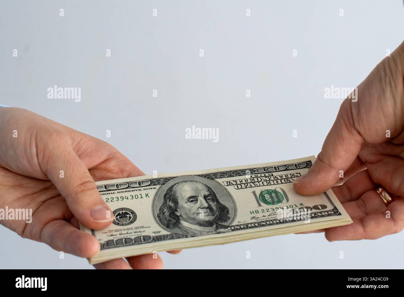 Close-up of two hands exchanging stack of US hundred dollar bills against neutral background. Concept of financial transaction, business deal, corrupt Stock Photo