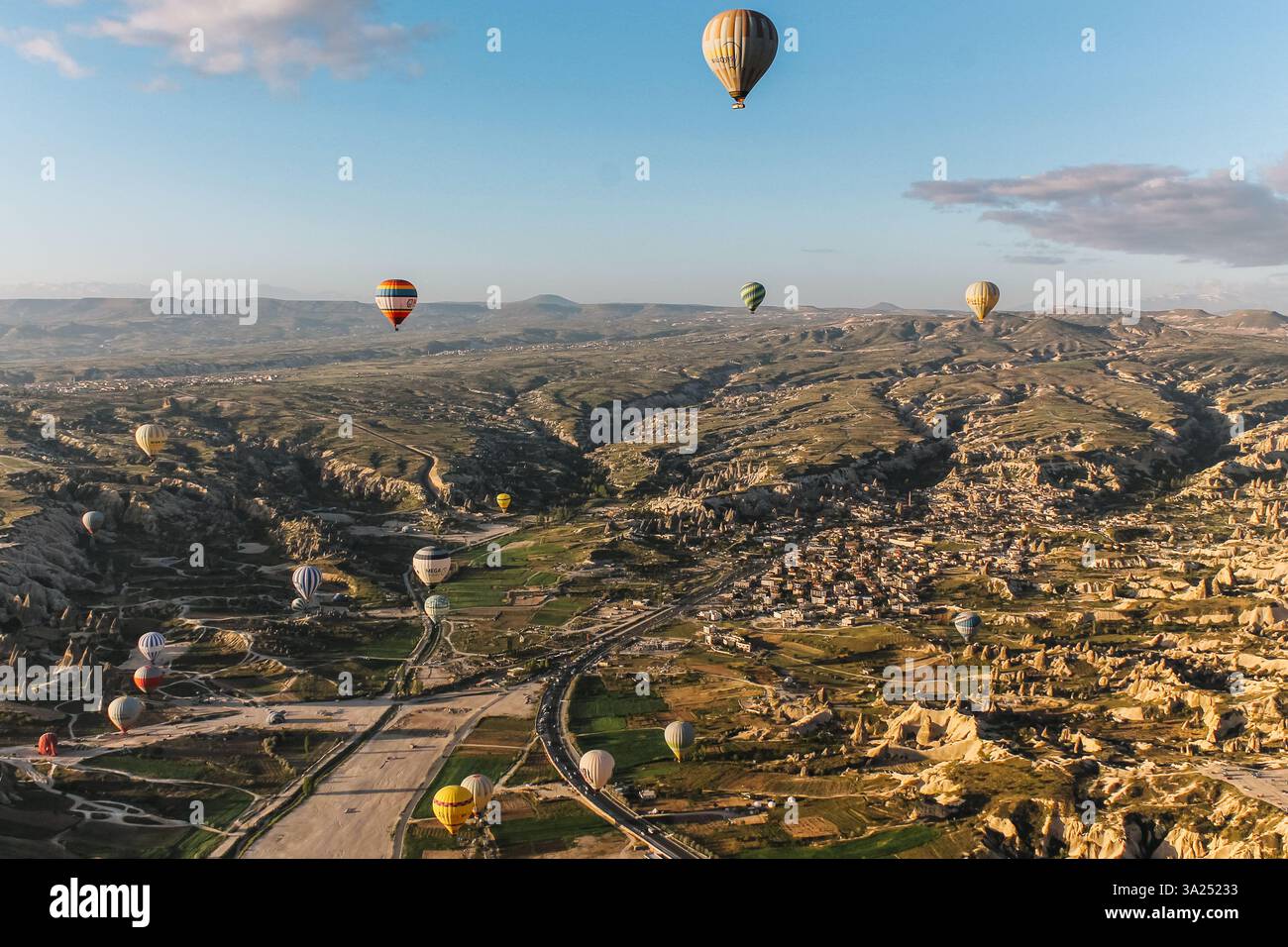 A group of colorful hot-air balloons floating above the rocky landscapes and open fields of Goreme, Cappadocia, Turkey, at sunrise. Stock Photo