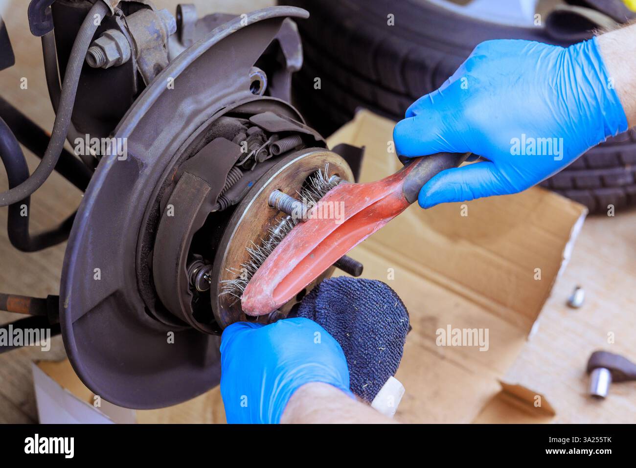 Hands equipped with gloves clean brake components in workshop setting while performing maintenance tasks car Stock Photo
