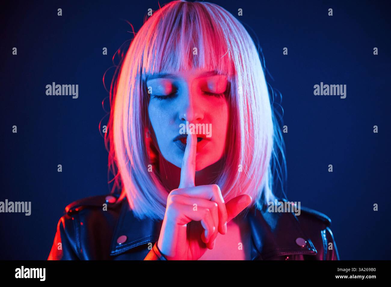 Finger by the lips, silence. Woman with white hair is in studio with neon colors. Stock Photo