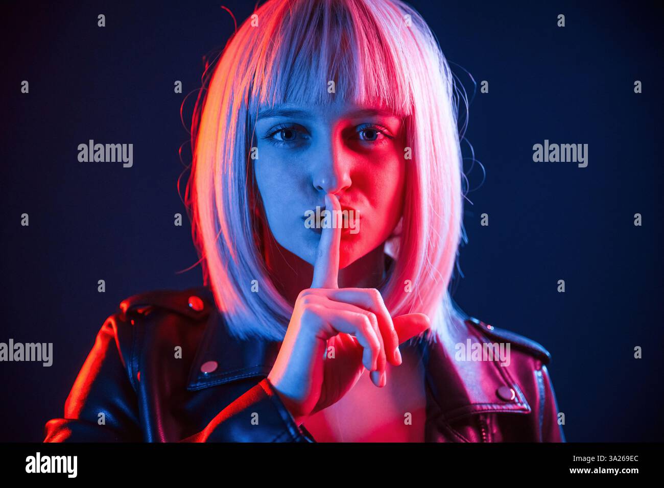 Finger by the lips, silence. Woman with white hair is in studio with neon colors. Stock Photo