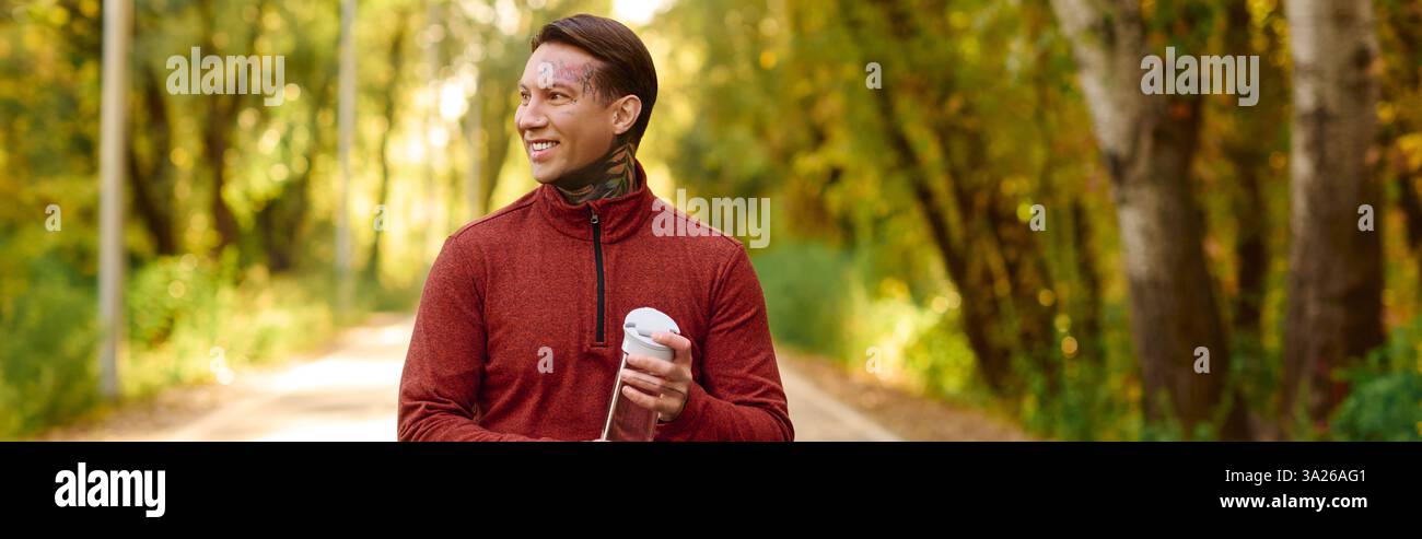 Handsome man with tattoos strolls down a tree lined path, showcasing a relaxed and modern style. Stock Photo