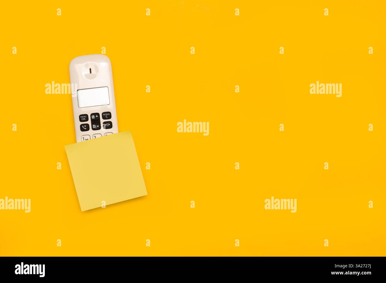 A blank yellow sticky paper over a telephone handset on a yellow background with copy space Stock Photo