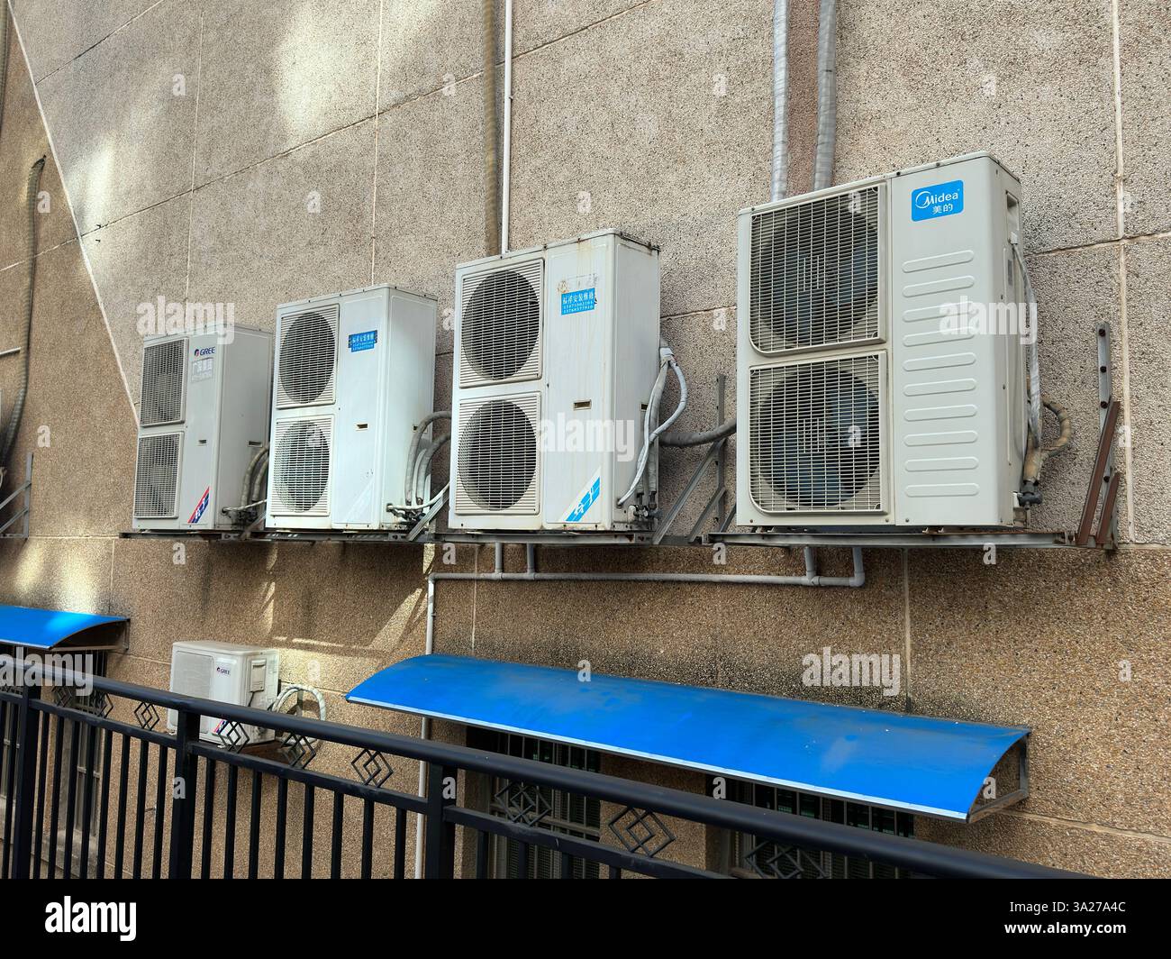 A collection of air conditioning units attached to a building's facade, showing fans and a blue shade. - Smartphone Captured Stock Image
