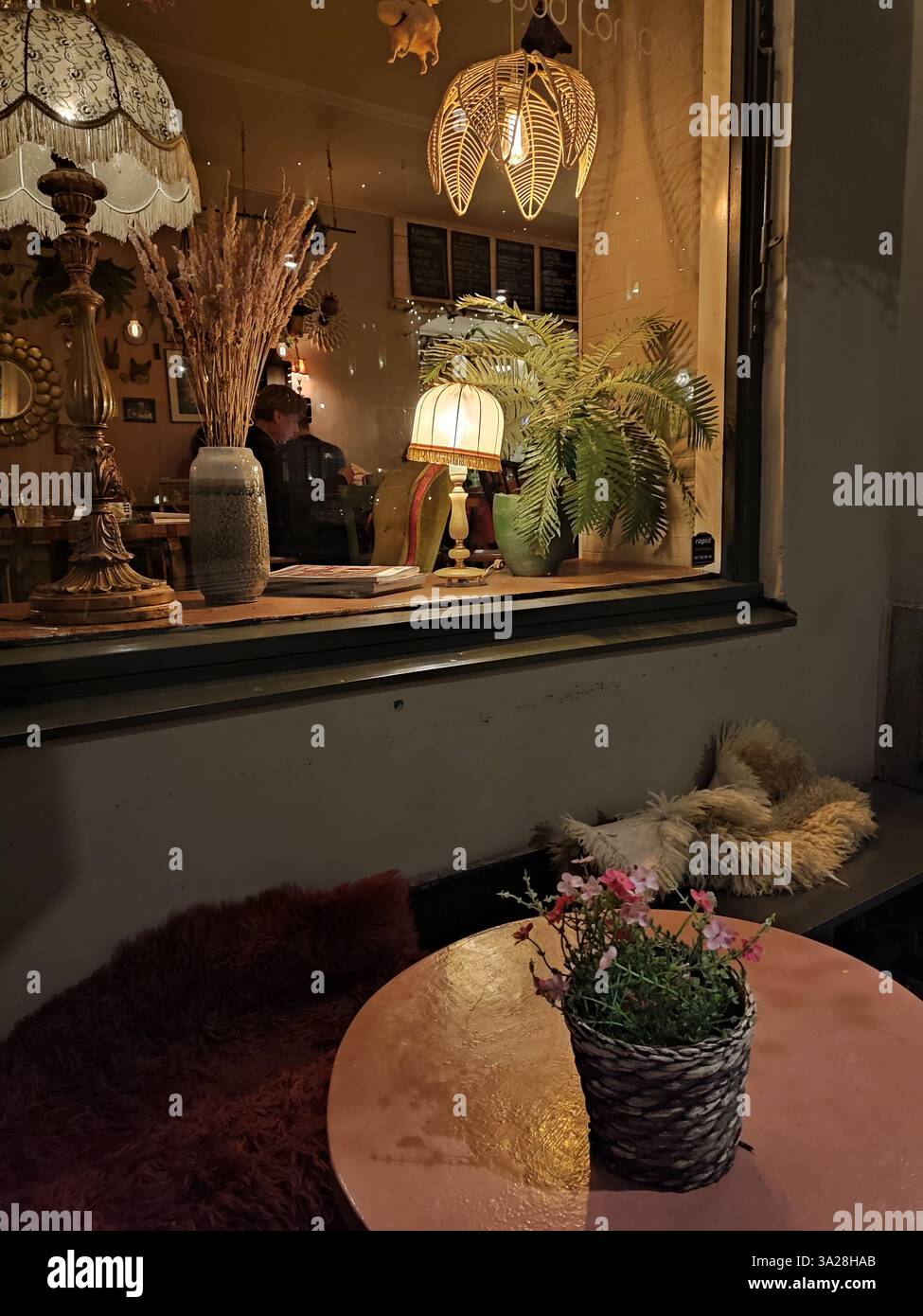 Warm and cozy café interior with lamps and vintage decors, viewed through the window in the autumn evening in Stockholm, Sweden - Smartphone Captured Stock Image